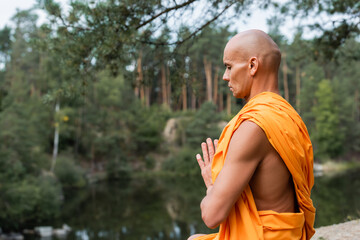 side view of buddhist with closed eyes meditating with praying hands in forest