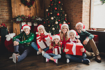 Canvas Print - Portrait of attractive cheerful family wearing hats holding December presents sitting on floor tree at home loft house indoors