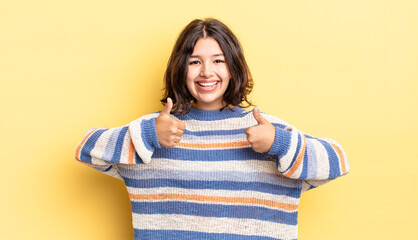 Wall Mural - young pretty girl smiling broadly looking happy, positive, confident and successful, with both thumbs up