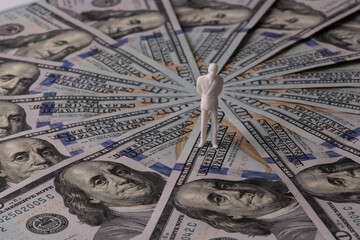 A symbolic plastic figurine of a man stands on the 100 USD bills