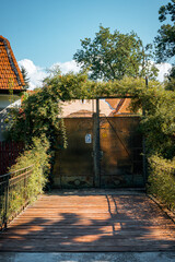 Poster - Wooden road with metal fences on sides leading to a mesh gate with plant arch