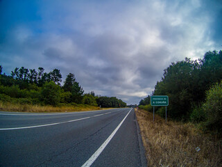 Poster - View of the highway surrounded by grass, plants and trees and the street sign on a gloomy day