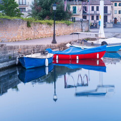 Wall Mural - two boats and street lighter with reflections in water in city Capodimonte in Lazio in Italy