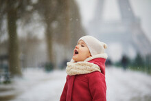Adorable Toddler Girl Catching Snowflakes With Her Tongue Near The Eiffel Tower In Paris