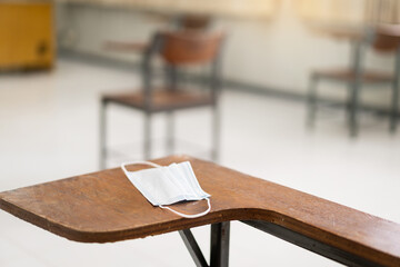 Poster - Used medical facemask on a wooden chair in an empty classroom during COVID-19 pandemic