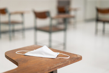 Poster - Used medical facemask on a wooden chair in an empty classroom during COVID-19 pandemic