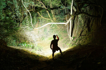 A trail runner using a flashlight in dark forest