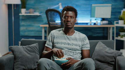 Wall Mural - POV of person watching football game on television at home. Adult enjoying sports play and cheering to win while looking at camera and eating popcorn. Man relaxing with TV screen