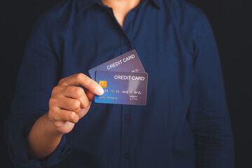 Midsection of a businessman in a blue shirt holding a mockup blue credit card while standing with a black background in the studio. Close-up photo. Money and business concept