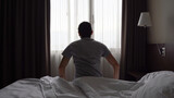 Fototapeta Sypialnia - Silhouette of lonely man sitting on bed in dark room by bedroom window. Depressed, early morning wake up, lazy, tired concepts