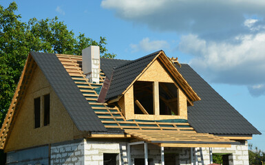 Wall Mural - Metal roofing construction. Metal roof tiles installation on a gable roof with attic windows and chimney of a house under construction.