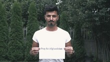 Pray For Afghanistan Sign. The 
 Muslim Afghan Man Is Holding A Sign To Save Afghanistan. A Piece Of Paper Request To Pray For Afghanistan