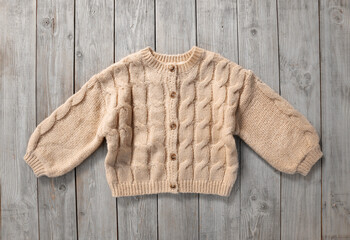 Wall Mural - Knitted pillover,beige color sweater on wooden background.Kid's farment,child's clothes, autumn winter clothing.Woolen wear.