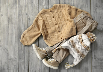 Wall Mural - Knitted cardigan, brown jeans and hat flat lay on wooden background. Baby autumn clothes. Boy's apparel set.Beige garment.Child's clothing top view.