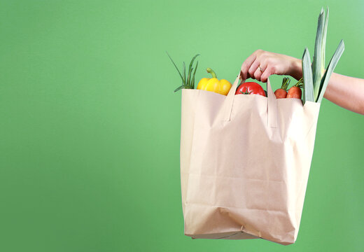 Hand holding paper bag with vegetables empty space green background.Online market,internet supermarket and orders.