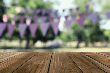 Empty wooden table in park decorated with bunting flags, space for design. Outdoor party