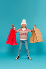 Wall Mural - child in warm sweater, jeans and sneakers standing with shopping bags on blue