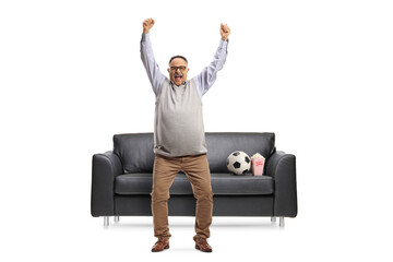 Sticker - Full length portrait of a happy mature football fan cheering in front of a sofa