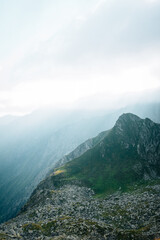 Wall Mural - Foggy sky over the peaks of a mountain range on the foreground of a rocky mountainside