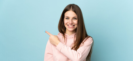 Wall Mural - Young caucasian woman isolated on blue background pointing to the side to present a product