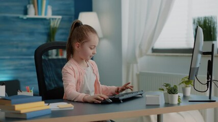 Wall Mural - Pupil using keyboard and computer for online class lessons at desk. Young girl looking at monitor for school task and homework. Little child working on pc for remote education and knowledge