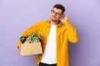 Young caucasian man making a move while picking up a box full of things isolated on purple background having doubts