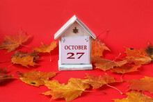 Calendar For October 27 : Decorative House With The Name Of The Month In English, The Number 27, Autumn Maple Leaves On A Red Background, Side View