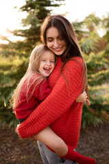 happy woman hold little kid girl 3-4 year old wear red bright sweaters posing over nature background