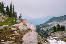 Male Hiker And Dog Standing On A Cliff In The North Cascades