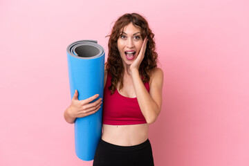 Young sport woman going to yoga classes while holding a mat isolated on pink background with surprise and shocked facial expression