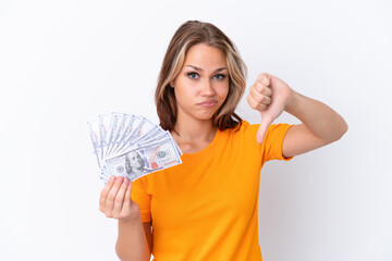 Wall Mural - Young Russian girl holding dollars isolated on white background showing thumb down with negative expression