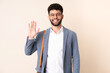 Young business Moroccan man isolated on beige background saluting with hand with happy expression