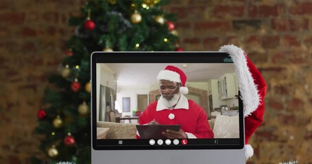 Sticker - Senior african american man in santa costume on video call on computer, with christmas tree