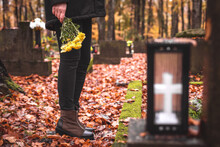 Mourning Woman Holding Flowers In Hands And Standing At Grave In Cemetery. Sadness And Grief During Funeral