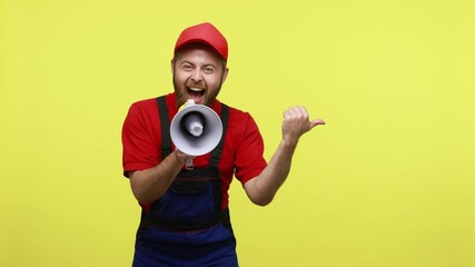 Wall Mural - Extremely happy worker screaming loud in megaphone and pointing aside, announcing advertisement, wearing blue uniform, red T-shirt and visor cap. Indoor studio shot isolated over yellow background.