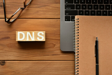 Poster - On the table there is a word cube lined DNS with laptop computers and glasses. It is an abbreviation for the word Domain Name System.