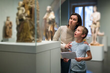 Attentive Young Woman With School Age Boy Visiting Sculptures Exposition In Museum
