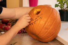 Man Is Carving Orange Pumpkin On Wooden Table. Creative Person Setting Mood For Trick-or-trickers. Halloween Is Here
