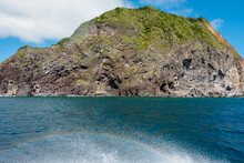 The Waves Of The Yacht Next To The Island Reflect A Short Rainbow