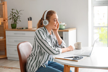 Wall Mural - Young woman with laptop video chatting in kitchen