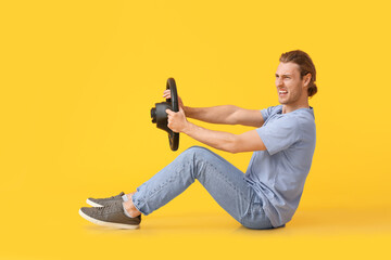 Angry young man with steering wheel on color background