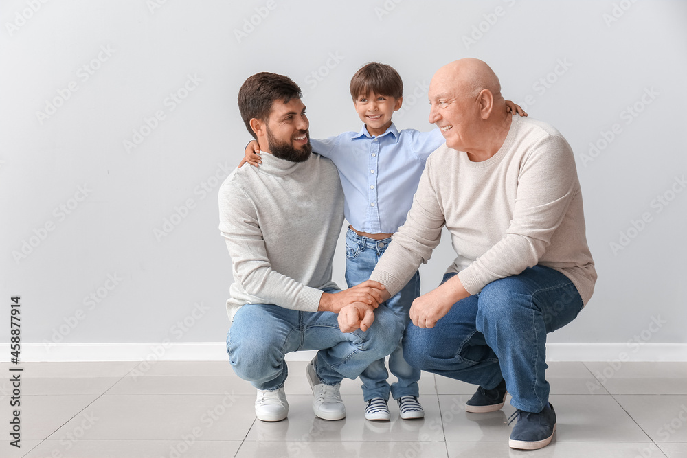 Happy man, his little son and father near light wall