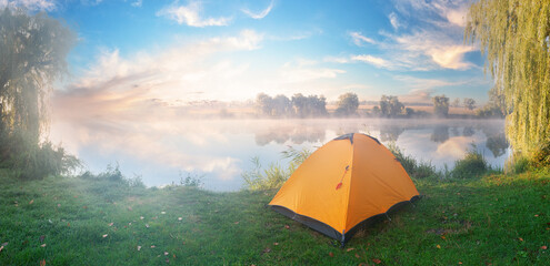 Wall Mural - orange tent on bank of river covered with fog in early morning