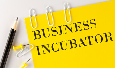 Poster - BUSINESS INCUBATOR word on the yellow paper with office tools on white background