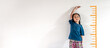 An adorable Asian little child girl measuring the height growth with the orange drawing on the white wall background. Girl power future and dream concept idea. Copy space