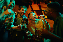 Cheerful Friends Having Fun While Singing Karaoke During Their Night Out In A Pub.