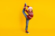 Full size photo of small happy girl cheerful flexible raise leg xmas isolated on yellow color background