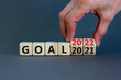 © Dzmitry - Planning 2022 goal new year symbol. Businessman turns a wooden cube and changes words 'Goal 2021' to 'Goal 2022'. Beautiful grey background, copy space. Business, 2022 goal new year concept.