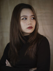 Poster - Vertical shot of a young Southeast Asian woman looking sidewards with wooden background in Vietnam