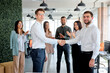 © alfa27 - Caucasian Young Business people co-workers colleagues greeting each other, shaking hands in modern office, side view on people in formal clothes, having successful partnership, men look at camera